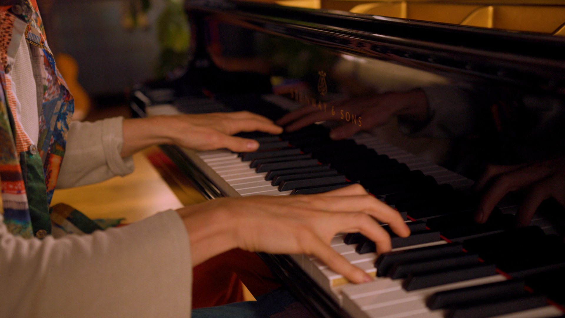 Close up of hands playing a a shiny black Steinway & Sons piano.