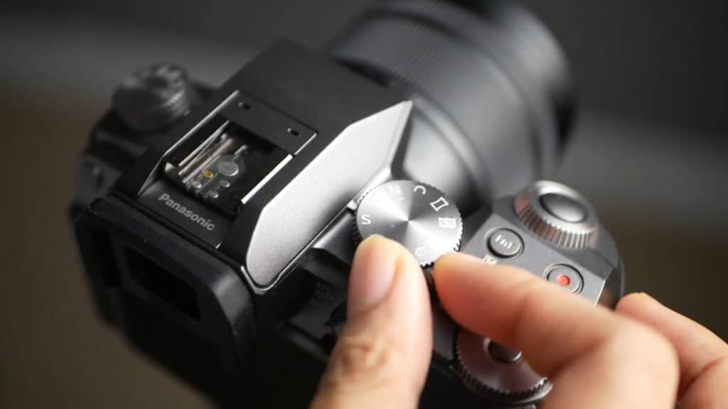 A person’s fingers touching the dial on top of a gray Panasonic DSLR camera.