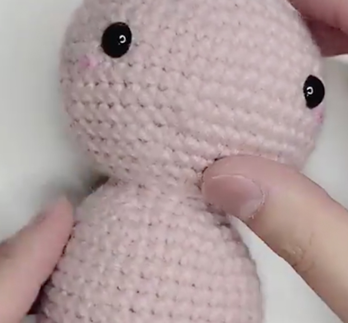 Light pink crochet amigurumi body with 2 black eyes on head.