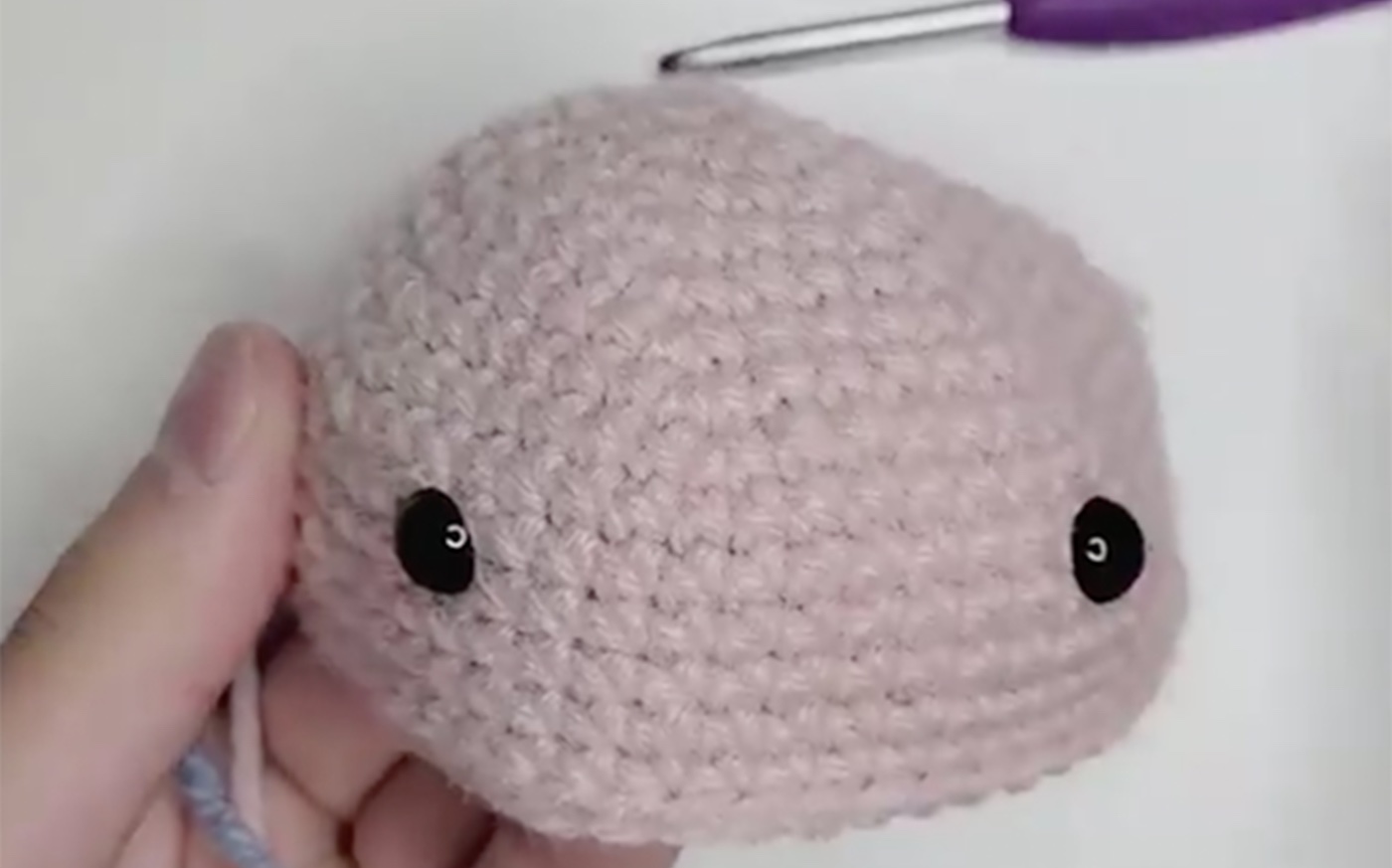 Light pink crochet amigurumi head with two black eyes.