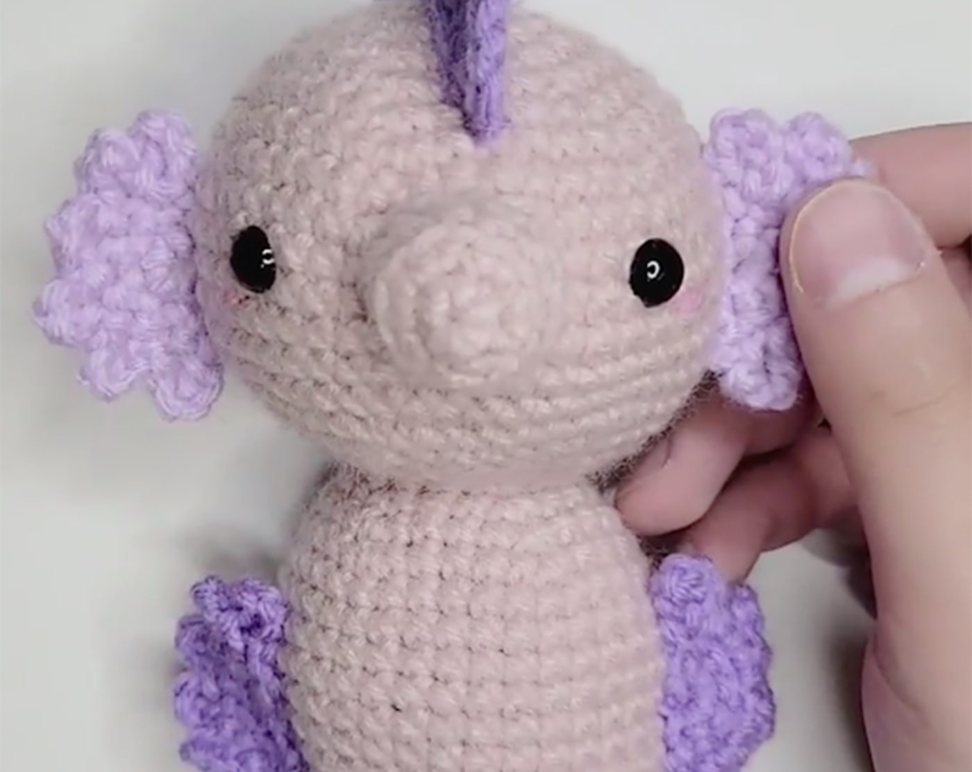 Amigurumi seahorse with light pink body and light purple fins.