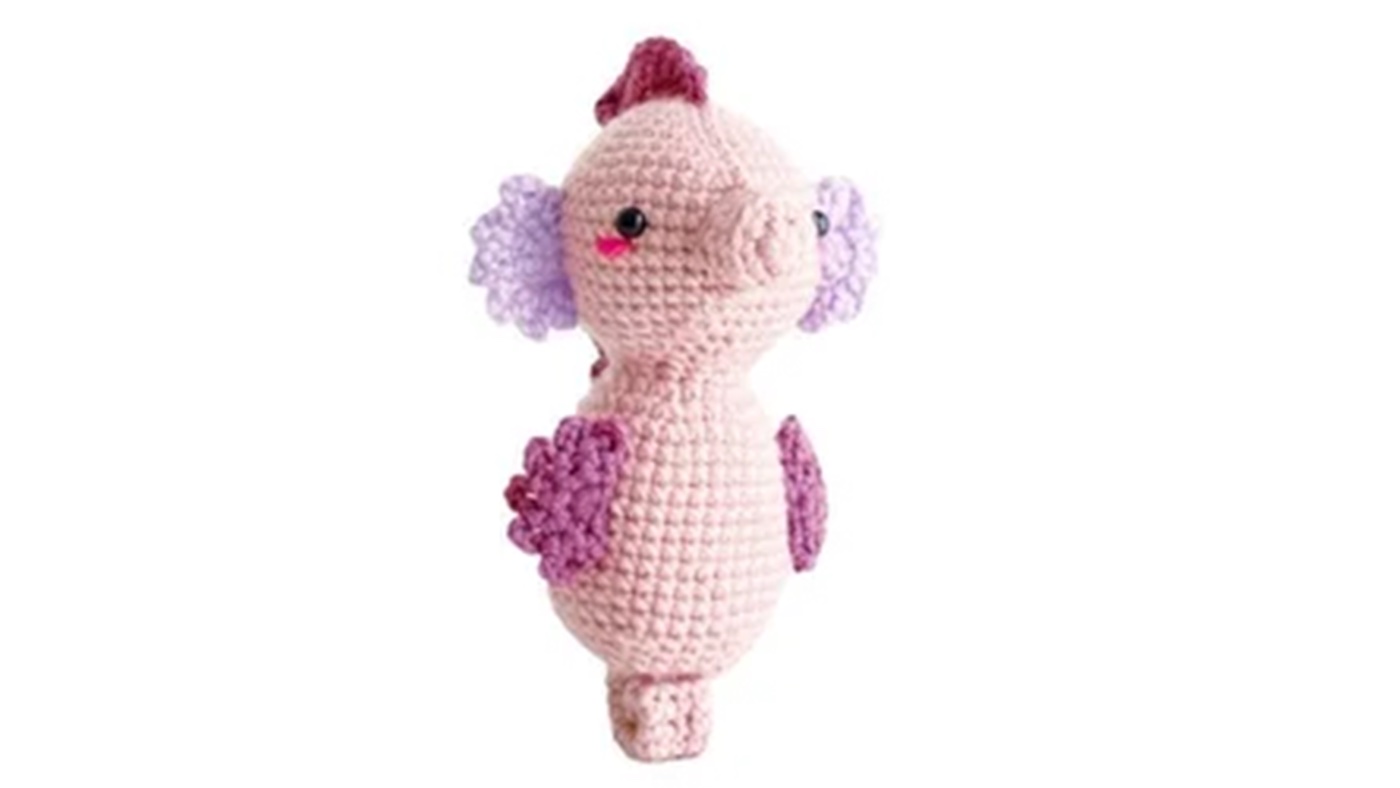 Amigurumi seahorse with light pink body and light purple fins..