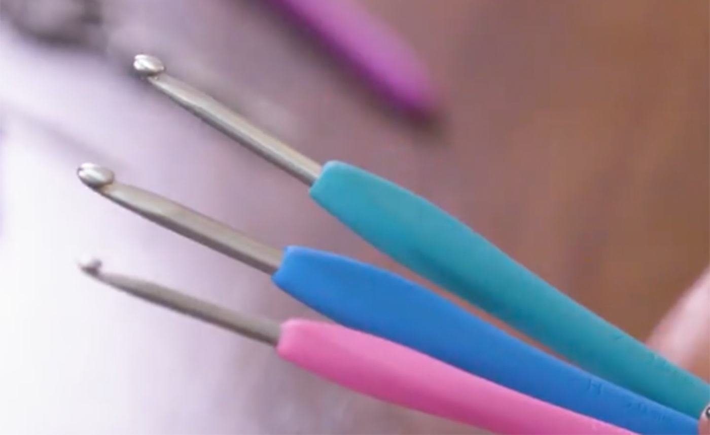 Three crochet hooks with pink, teal, and blue handles.