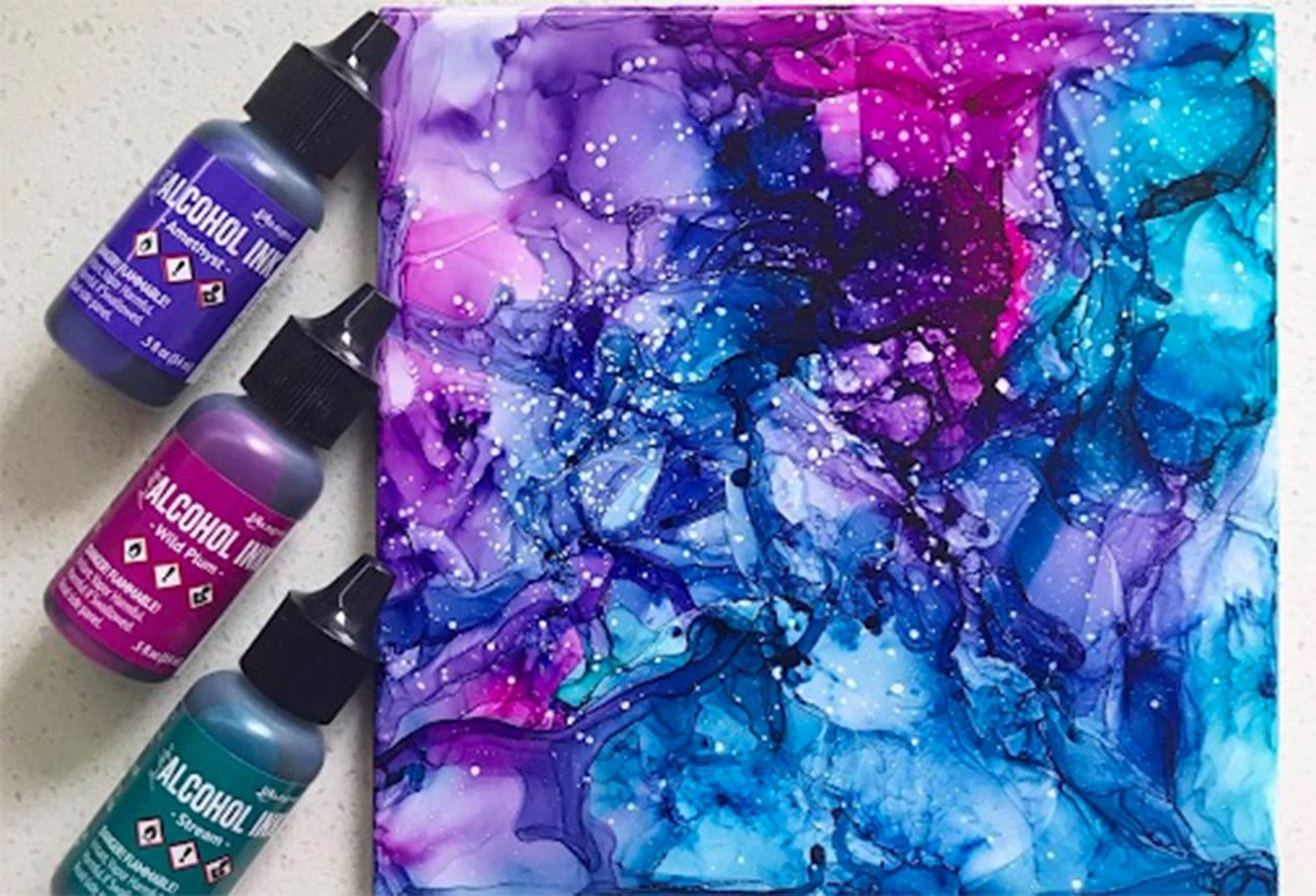 3 bottles of ink, purple, teal and pink on the left. And a finished alcohol ink with these colors on the right