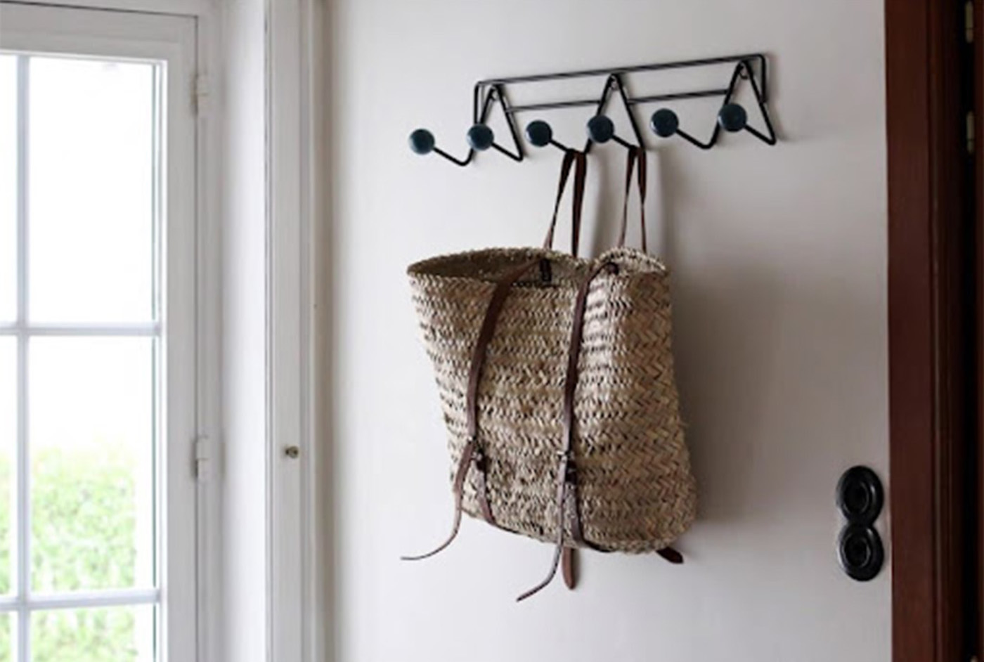 A woven bag hangs on a coat hanger on the wall next to a glass door.