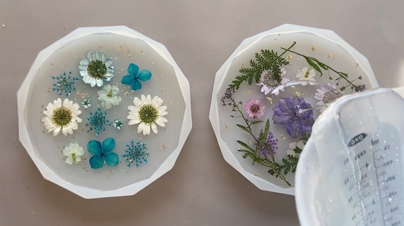 Pouring more resin over mold with flowers in it.