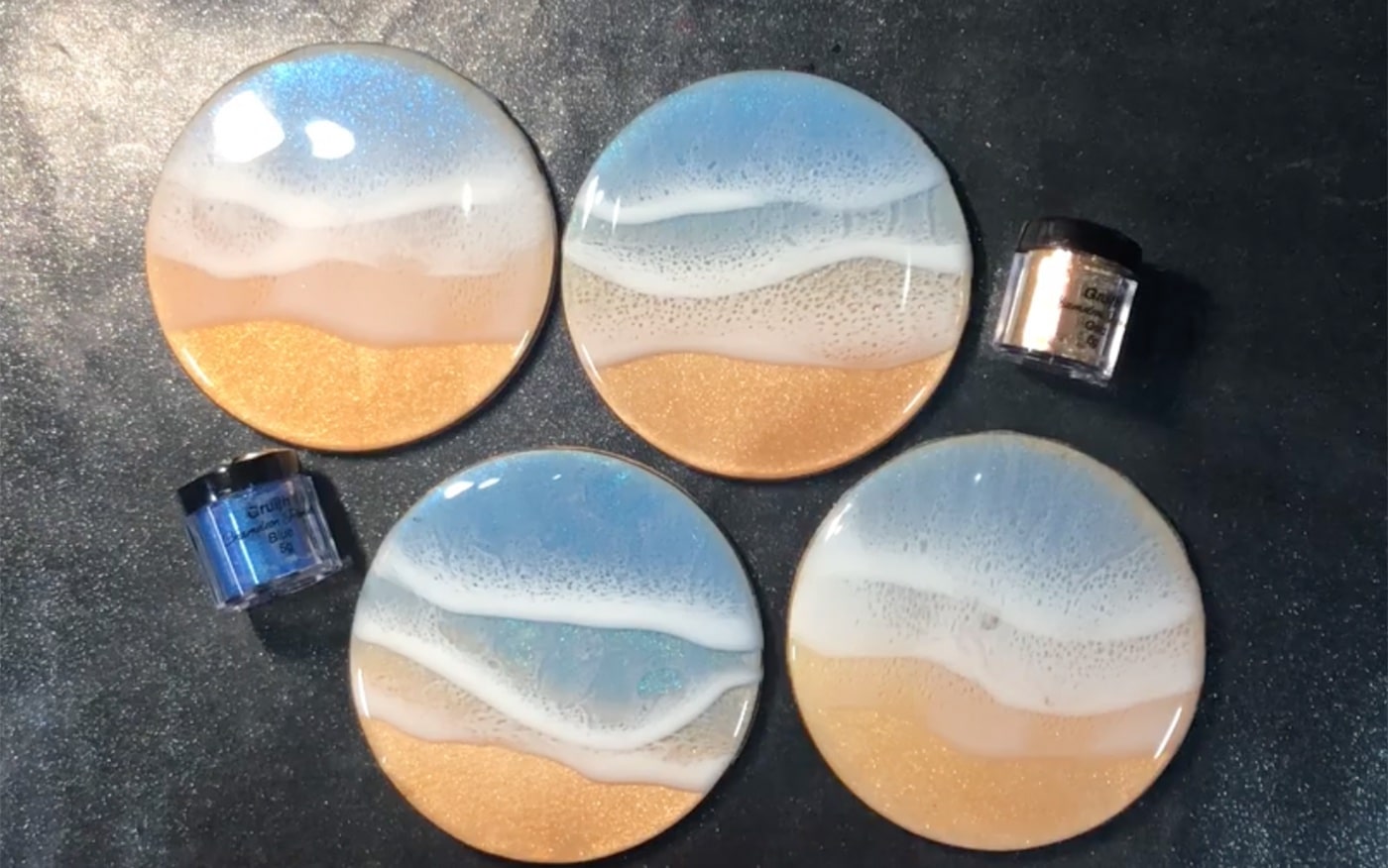 4 resin coasters that were painted to look like waves washing on a beach.