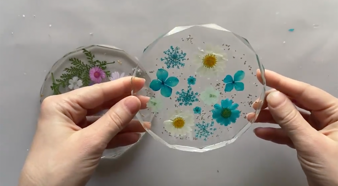 Hands holding finished clear resin coaster with flowers suspended in it.