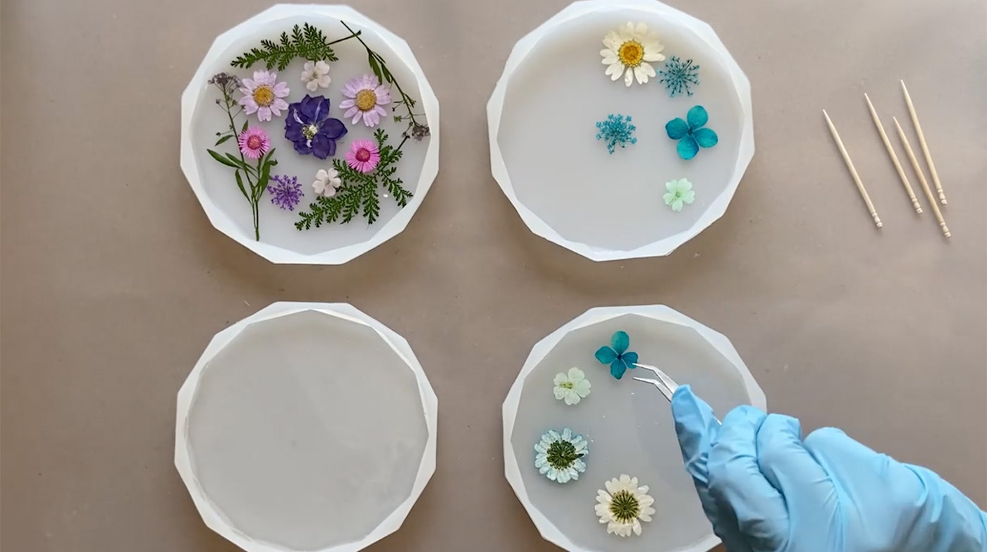 Person using tweezers to place dried flowers in half filled resin mold.