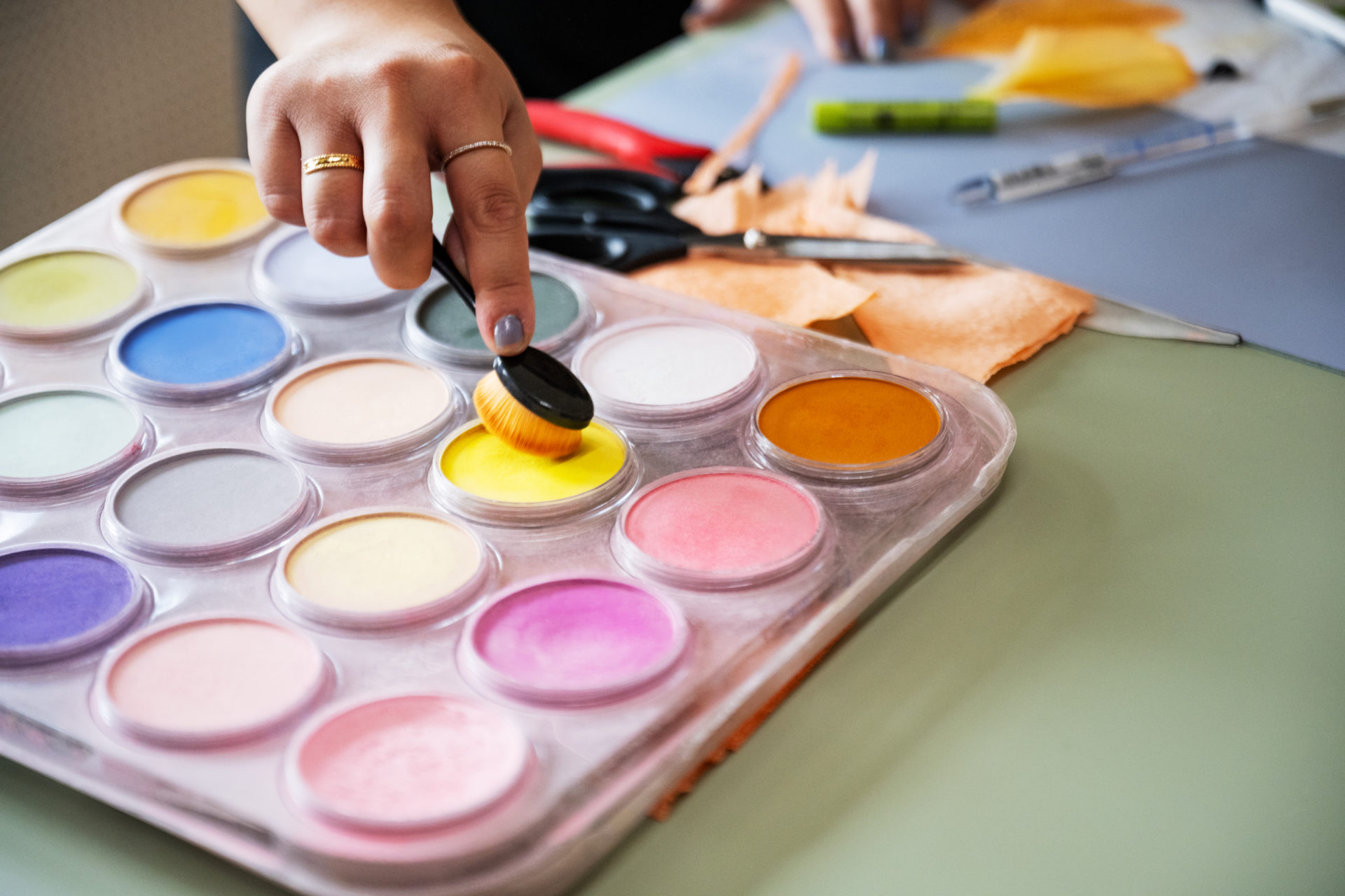 Artists brushing a paintbrush into a palette of chalk paints.