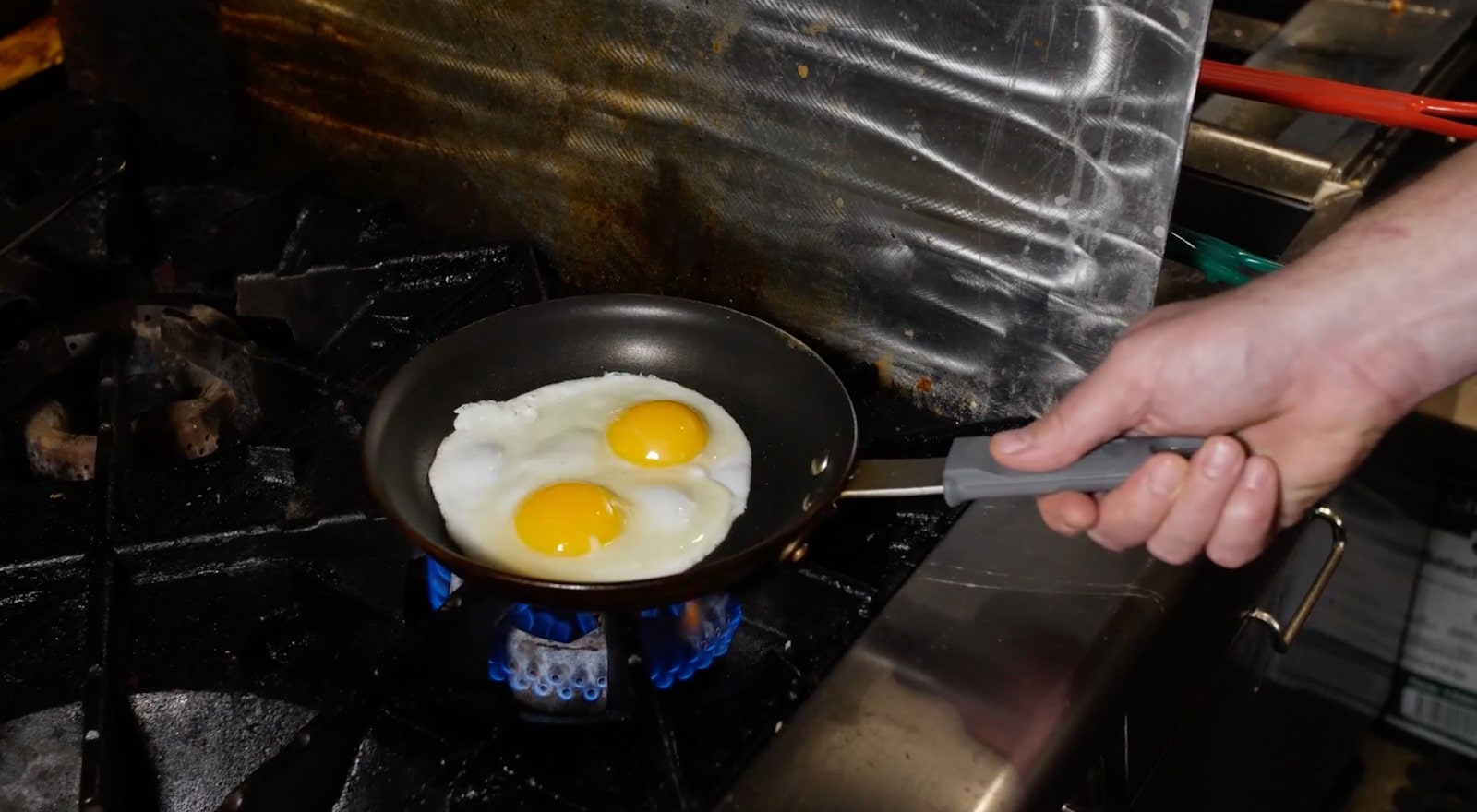 Two fried eggs sit in a small pan. The pan rests on a burner with a small flame blazing