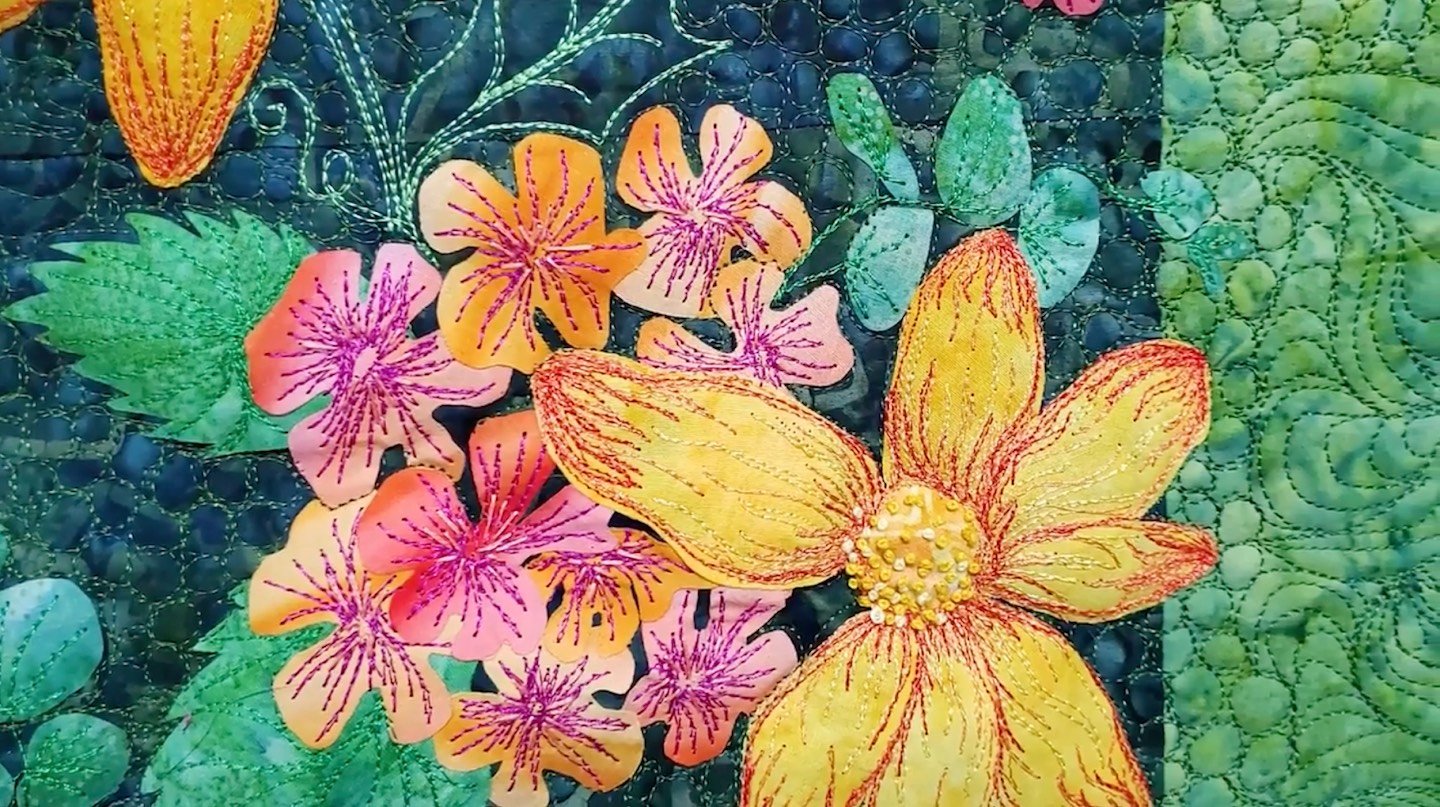 Yellow, pink and orange flowers are stitched onto a green background using red and magenta thread.