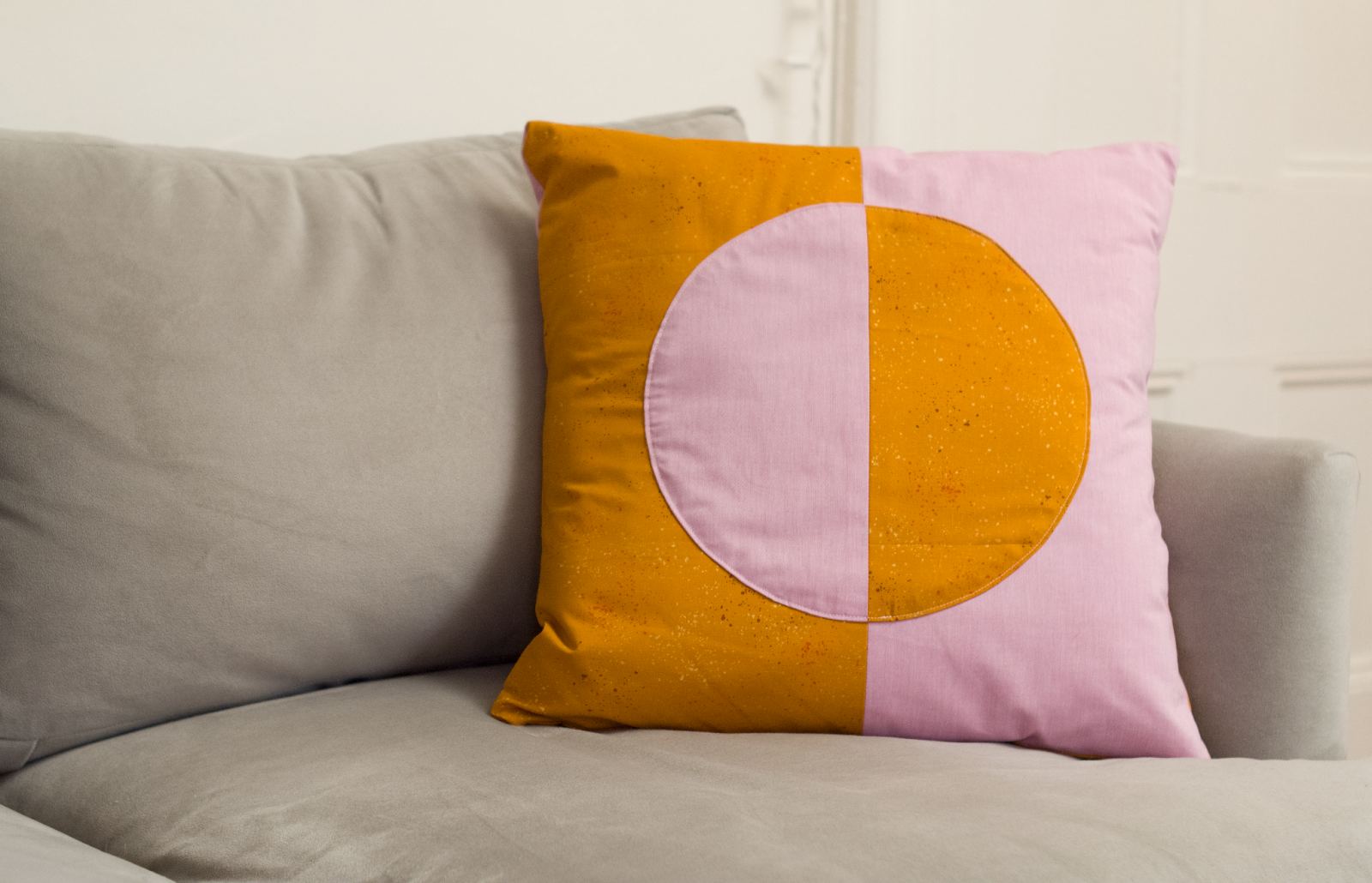 An orange and pink color-blocked pillow sits on a gray couch.