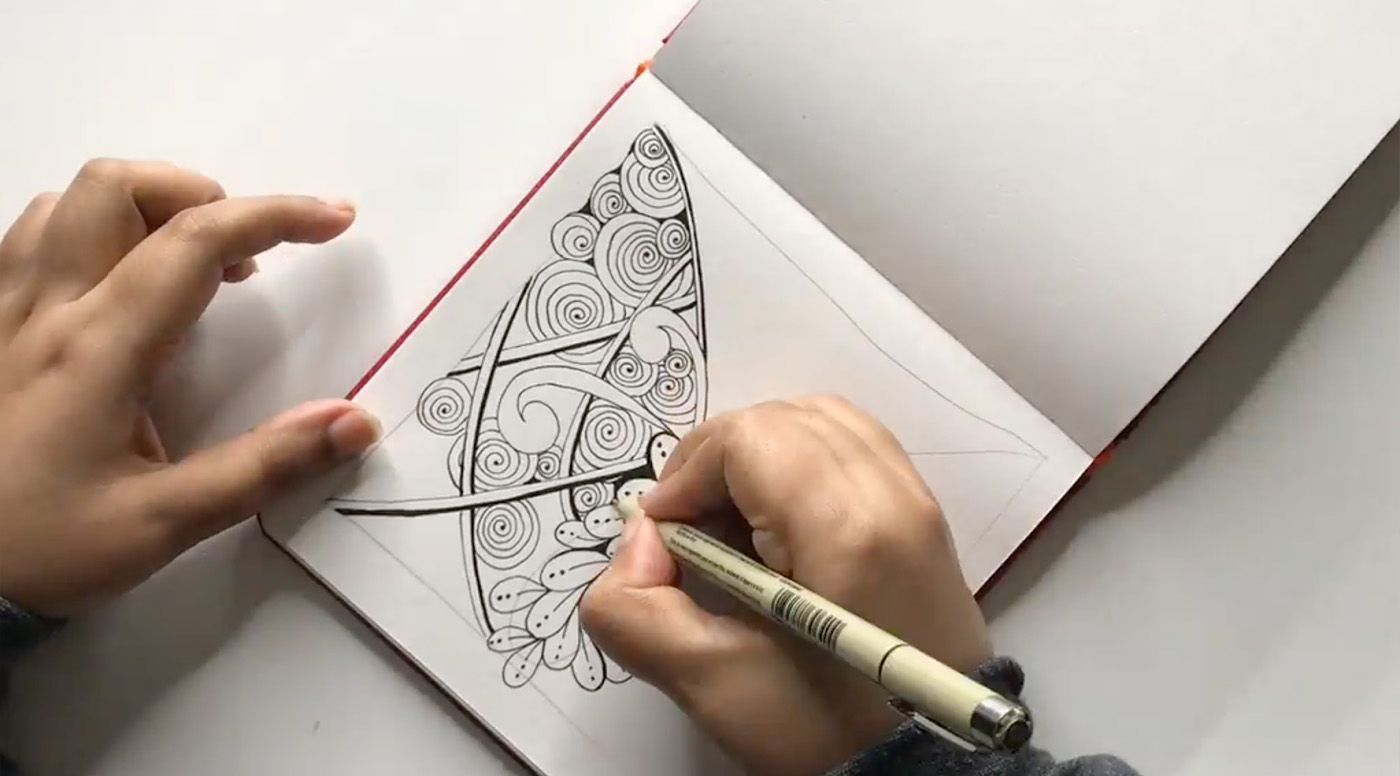 An intricate pattern of swirls and lines is drawn by an artist in a notebook. 