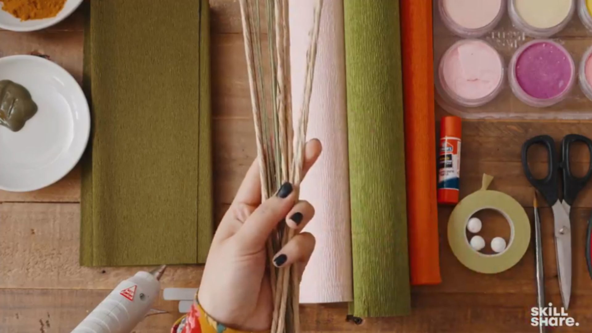 Person holding floral wire in their hand over a crafting table with supplies.