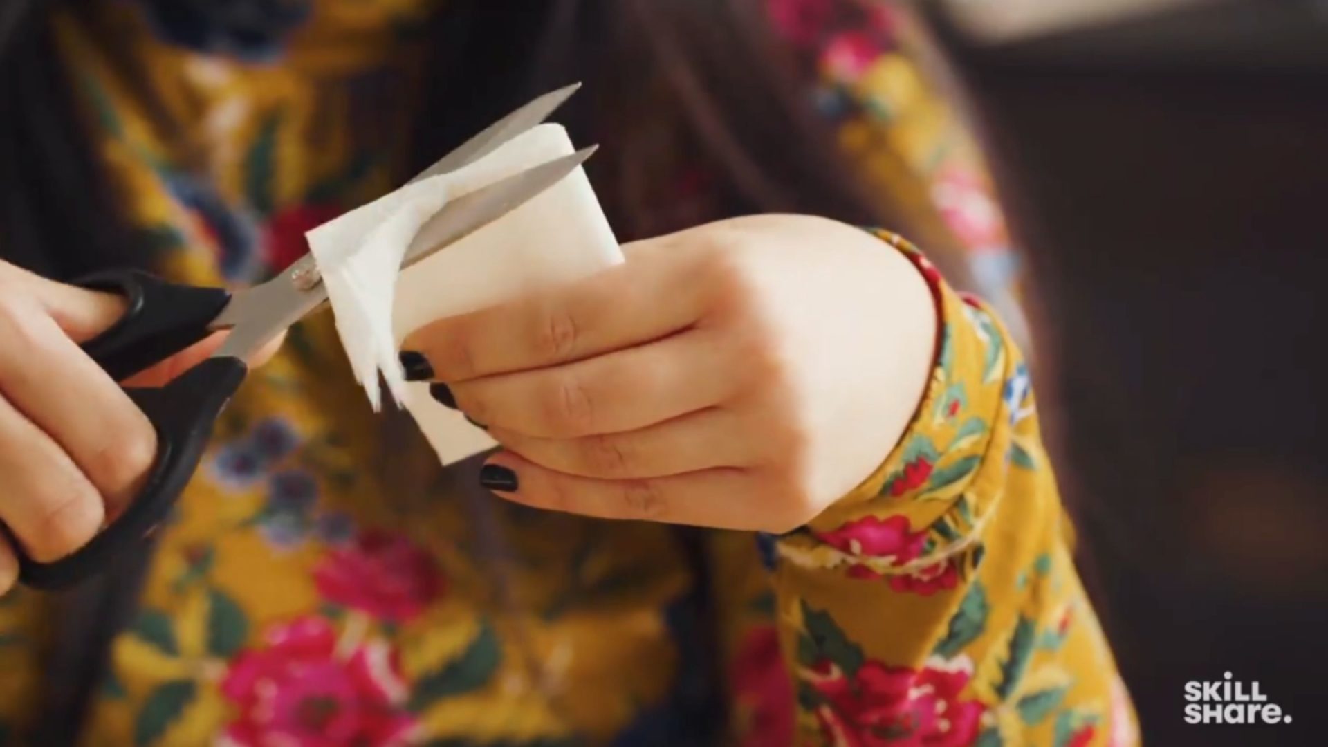 Person rounding off the edges of white crepe paper with scissors.