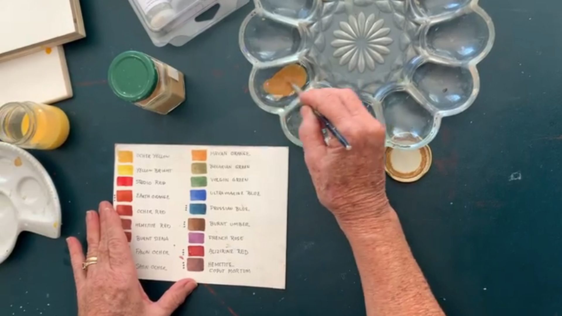 An artist mixing their paint in a flower-shaped palette, using their color chart as a guide.