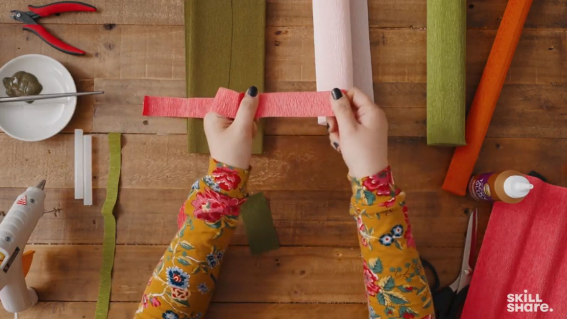 Person pulling red crepe paper above a crafting table.