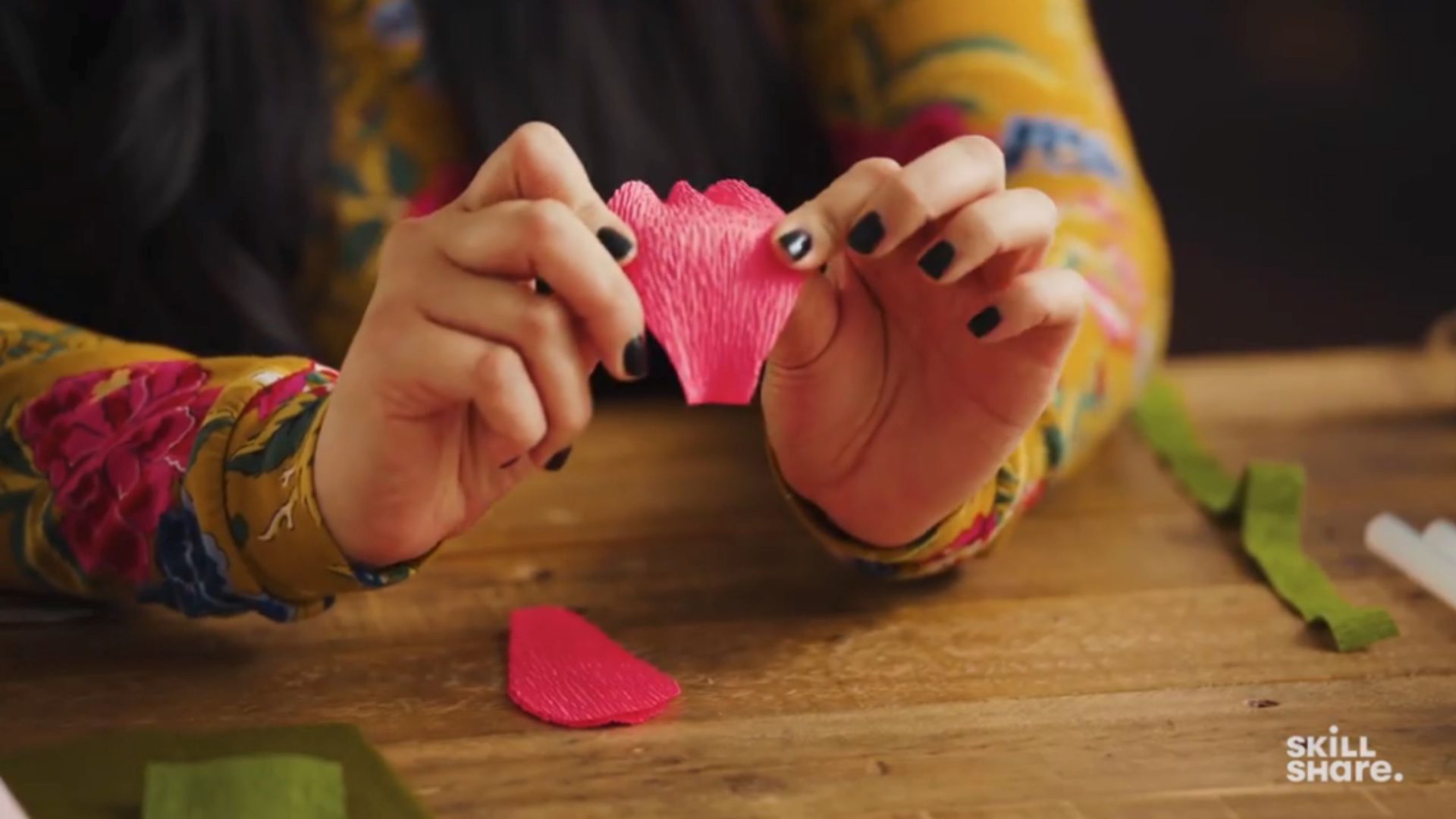 Two hands holding a piece of red petal-shaped crepe paper.