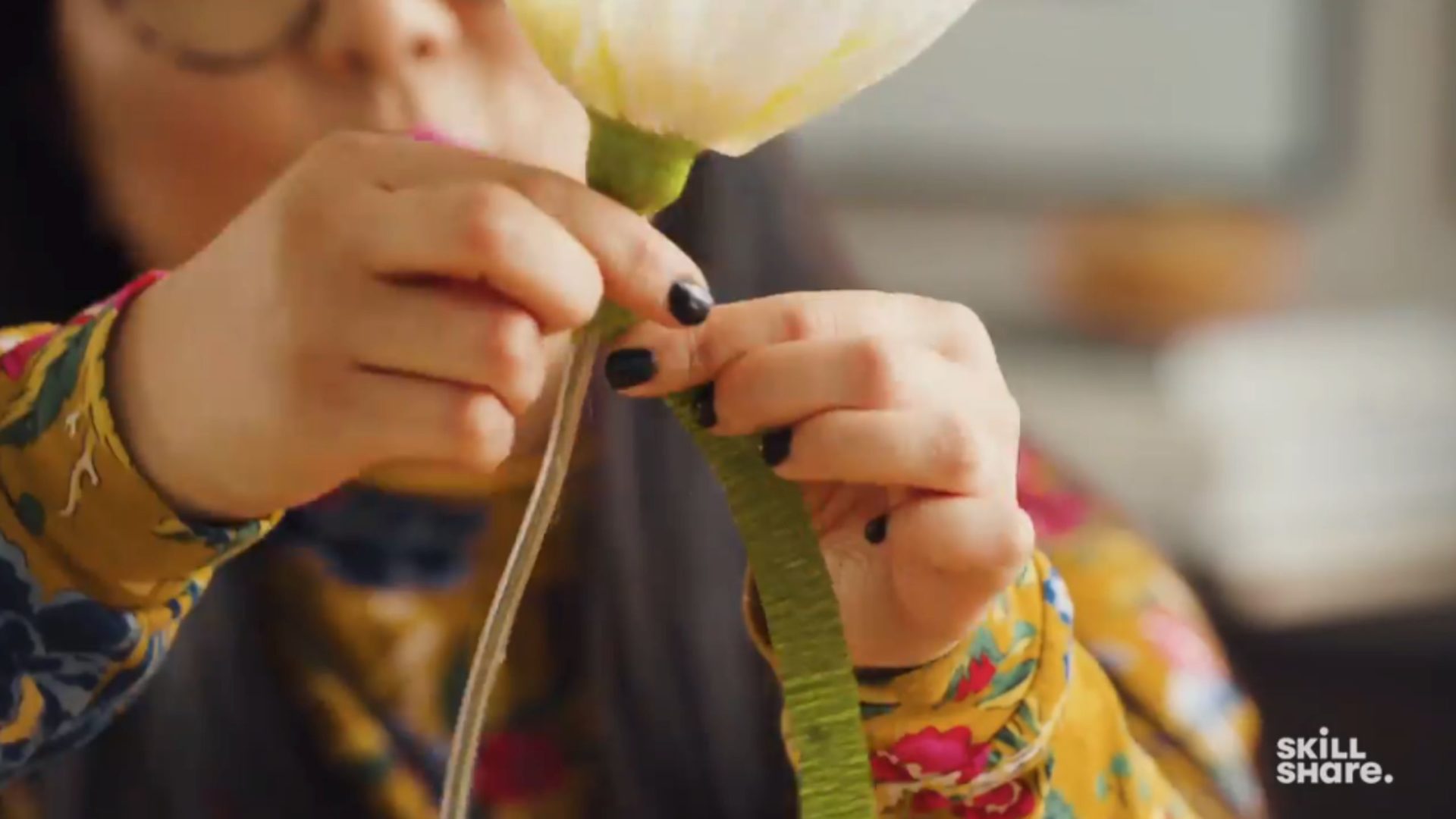 Person wrapping green crepe paper around a plastic tube and floral wire.