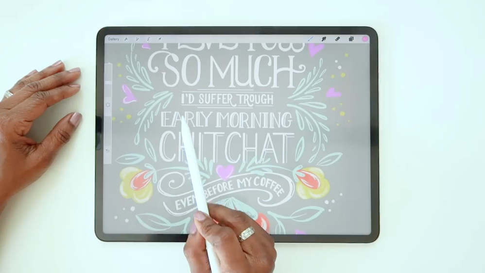 Two hands next to a tablet—one hand holds a stylus. The tablet features a portion of artful handlettering and includes  the phrase "...SO MUCH I'd suffer through early morning chitchat even before my coffee."
