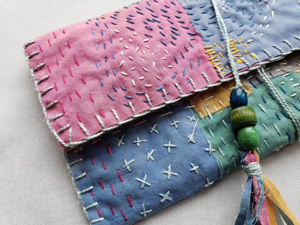Light pink, blue, green, and yellow patches of fabric cover this hand-crafted pouch with the help of Boro stitching.