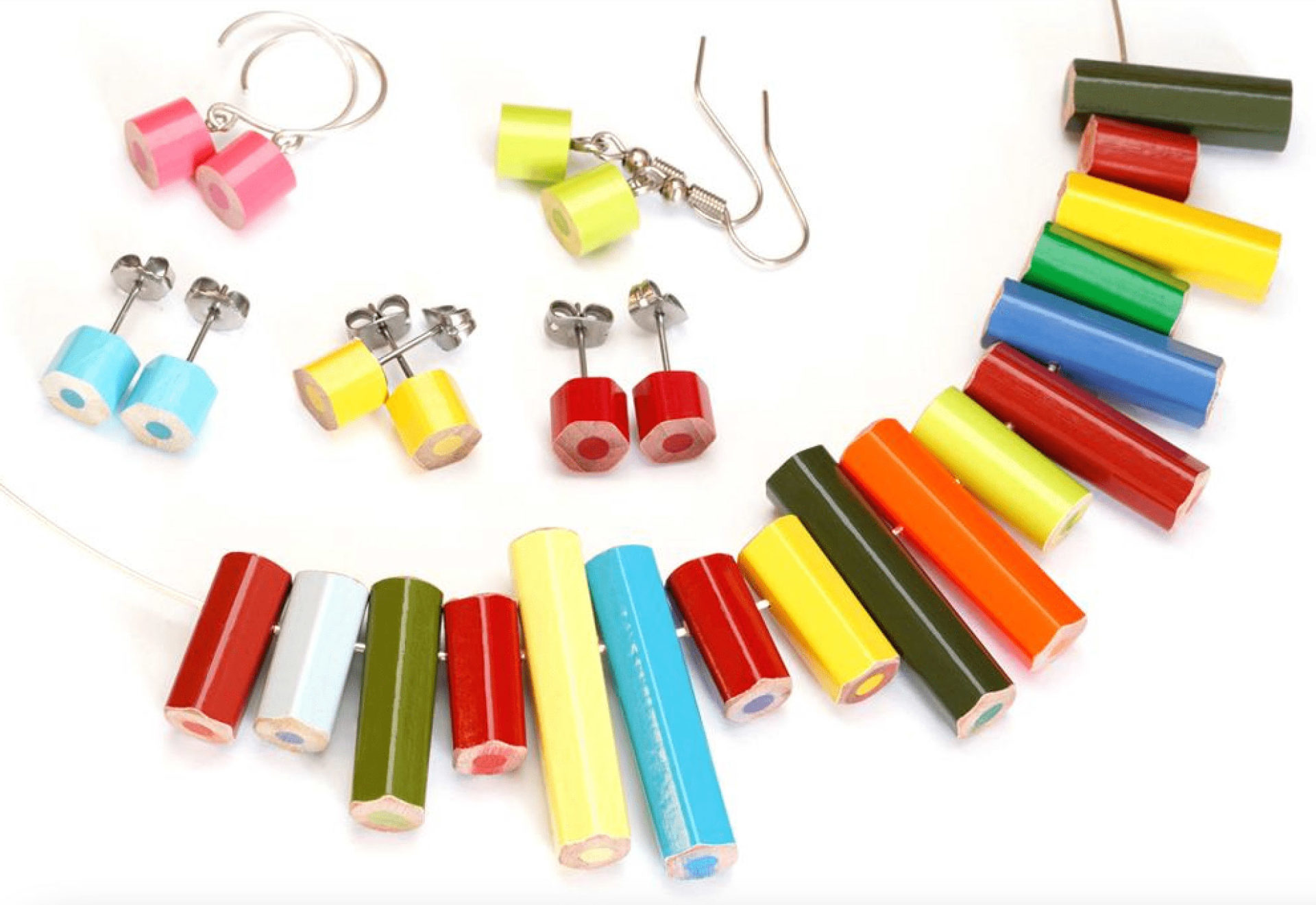 Two dangle earrings, three stud earrings, and a necklace sit on a white background. Each is made with a variety of colored pencil pieces that are red, white, green, yellow, and blue.