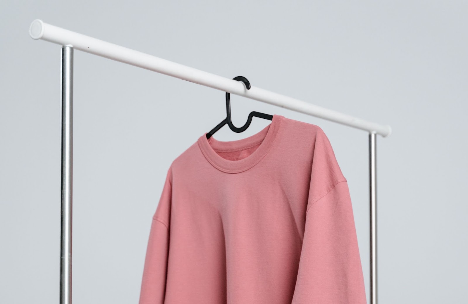 A pink sweatshirt hangs on a metal clothing rack.