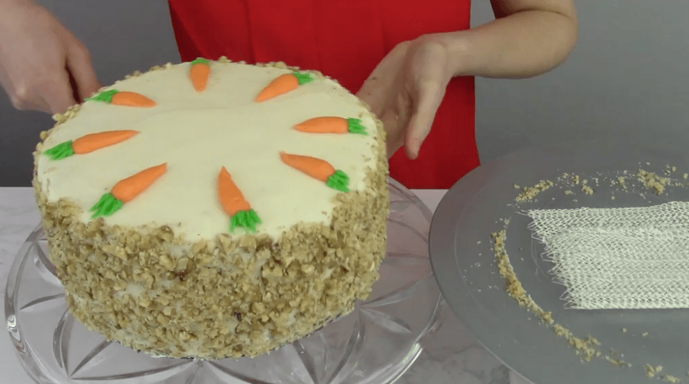 A finished carrot cake is placed onto a glass cake serving dish.