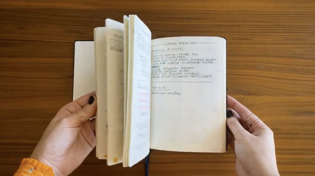 Hands holding an open bullet journal, which sits on a light brown wood surface.