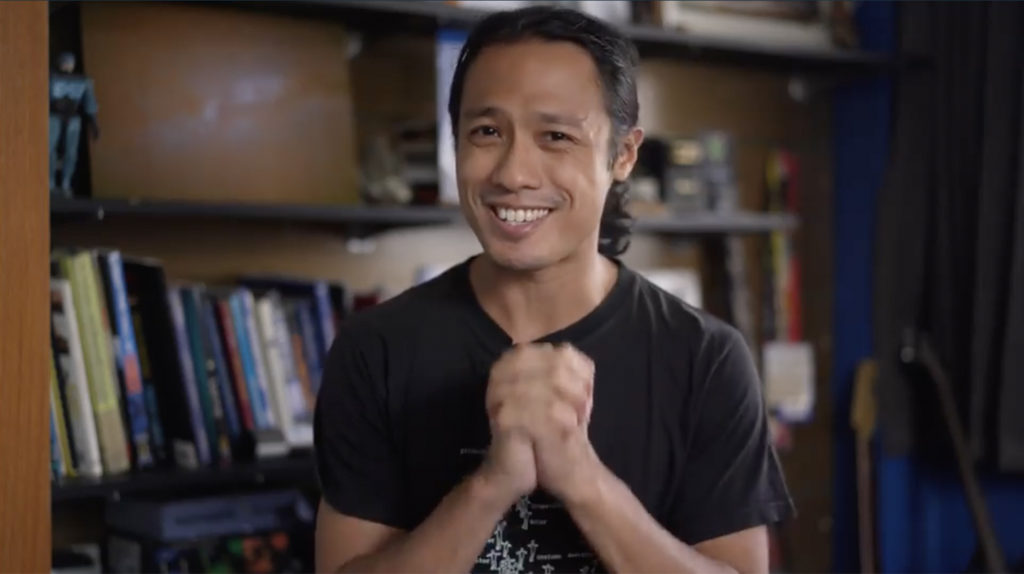 Skillshare teacher, Aaron Palabyab, sitting in front of a bookshelf, smiling, his hands clasped in front of his chest.