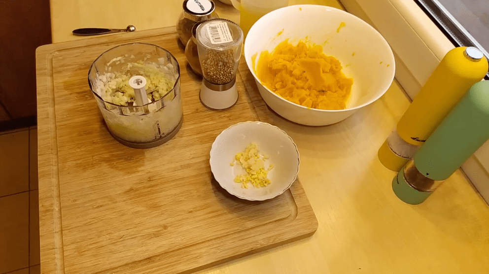 Pumpkin, onions and garlic in bowls and mixers on a wooden cutting board.