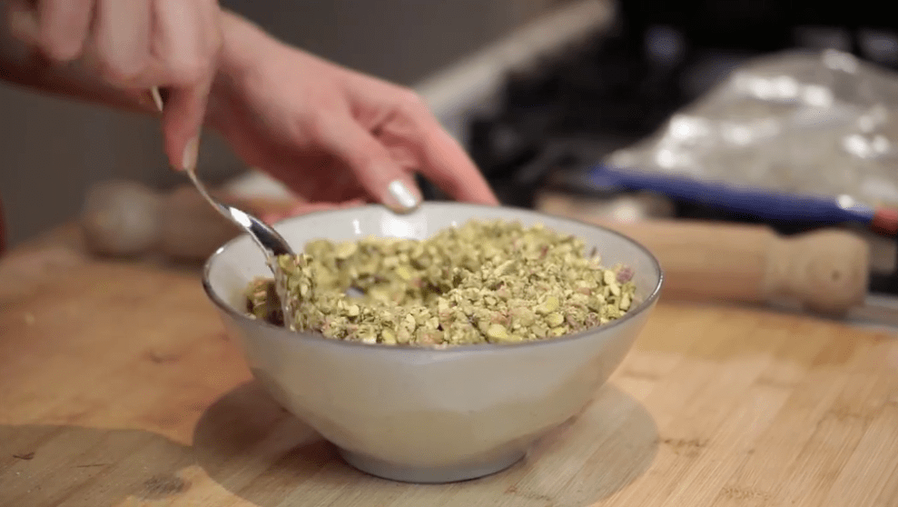 Chopped pistachios being mixed in a gray bowl on a wooden counter, ready to be made into baklava filling.