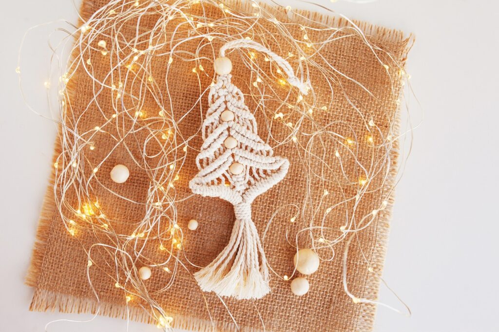 An elaborate macramé Christmas tree with intricate knots and wooden beads in the spine. It’s sat on top of hessian fabric and surrounded by fair lights to give a festive feeling.