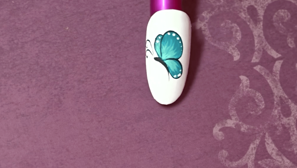 A fake nail with a teal butterfly design shows how detailed you can get with your nail art.