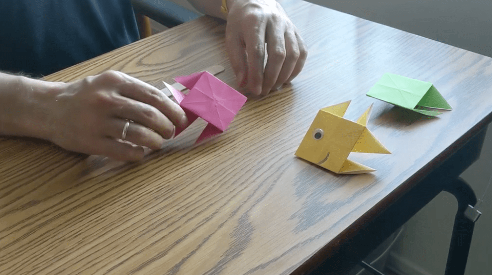 The pink origami fish is completed and sits on a table with a finished yellow paper fish.