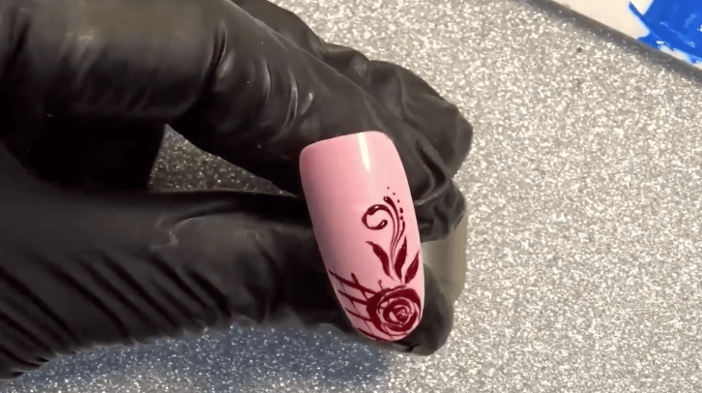 A pink fake nail with a rosebud and flower design, highlighting the level of detail each nail can have.