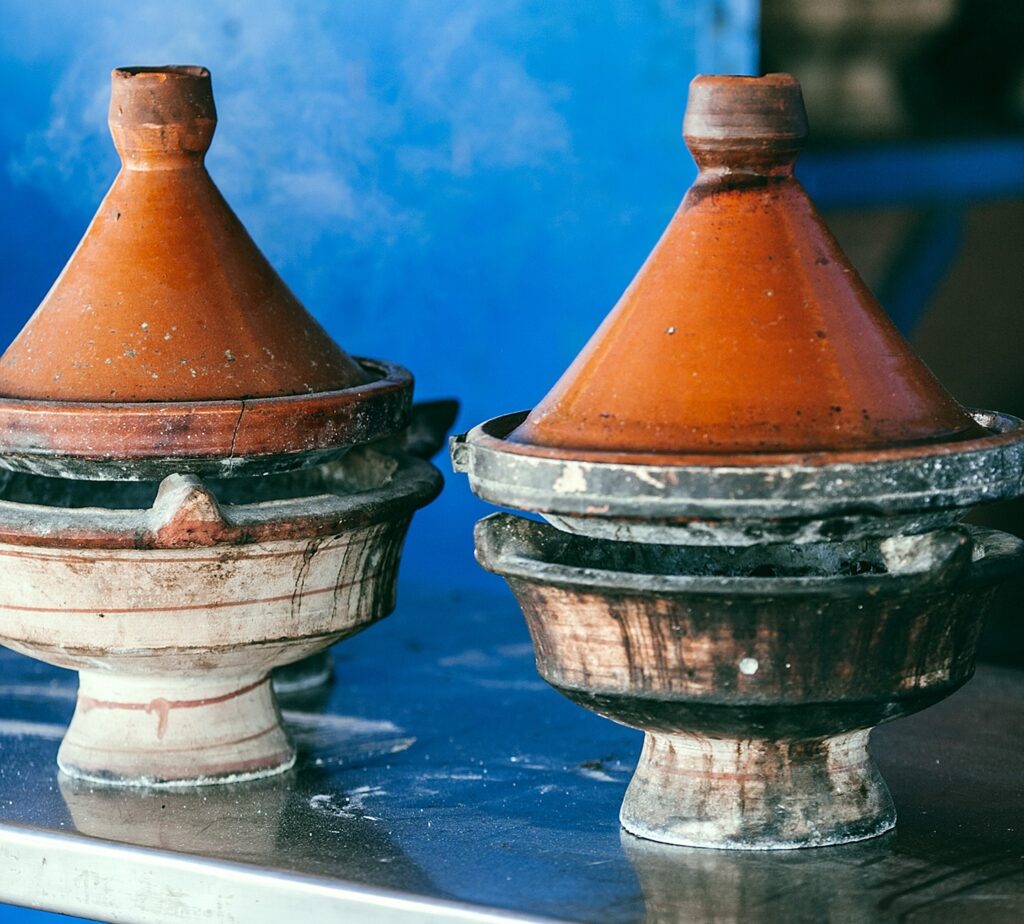 A photo of two tagines on a table. They have glazed tops and are suspended over a heat source.