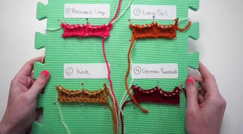 A woman’s hands holding a green styrofoam board, on which four knitting samples have been pinned. Each is labeled with the cast on method used to create it.