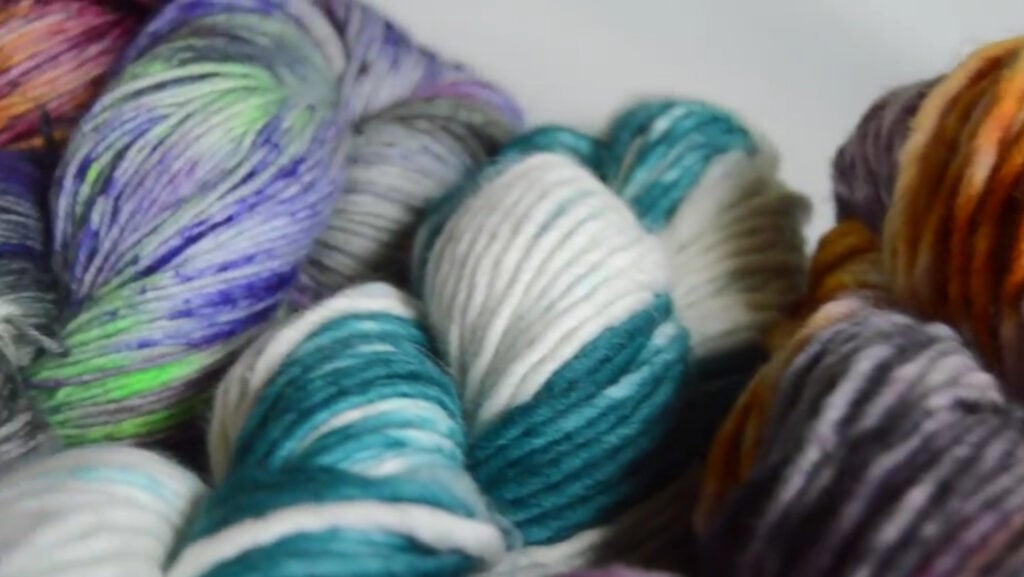 Multiple skeins of yarn in a myriad of colors, including blue, white, gray, orange, purple and green.
