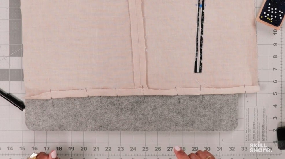 Cream material folded and pinned to create a crease needed for fabric hemming.