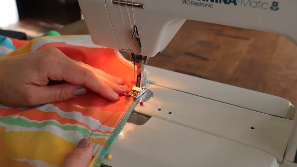 An orange, yellow, white and green fabric forming a hem as it passed under the needle of a sewing machine.
