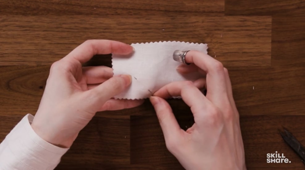 A needle being passed through white fabric to demonstrate a basic hand sewing technique.