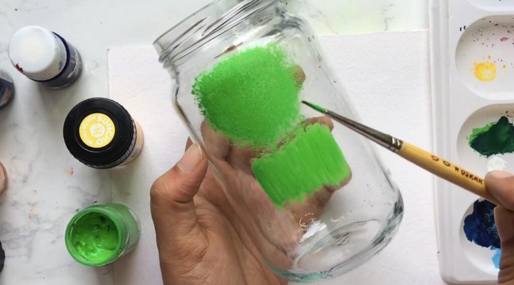 An empty glass jar with green paint applied by two different techniques to show the difference.
