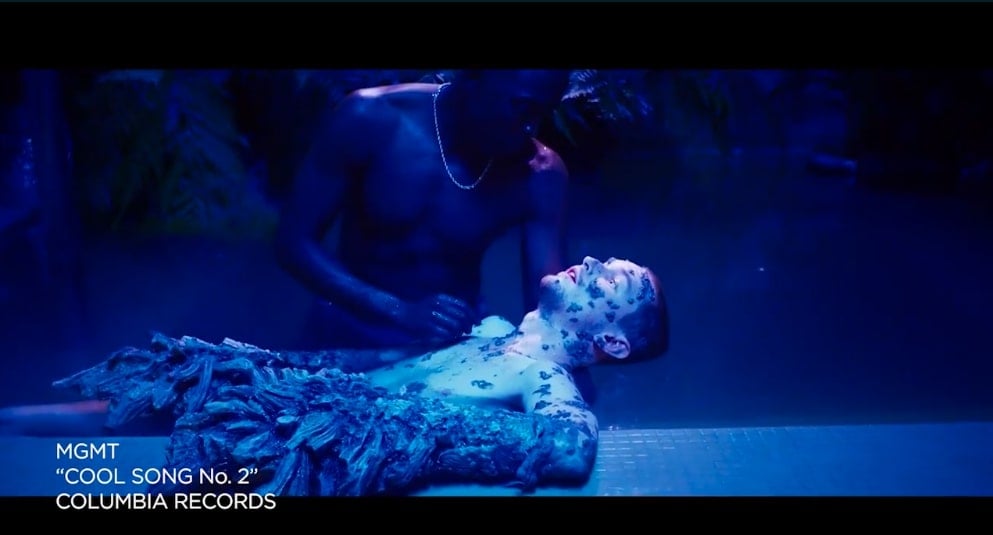 Two actors in a blue-lit room on the set of a music video.
