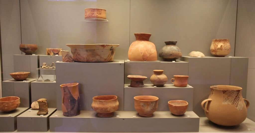 A range of ancient pottery vessels and bowls from the neolithic period, displayed behind glass at a museum.
