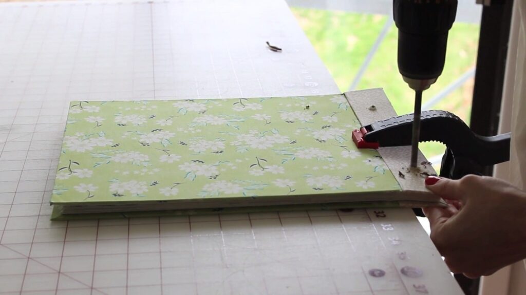 Skillshare teacher Bonnie Christine using a drill to make holes in the pages of her art portfolio so she can bind them together.