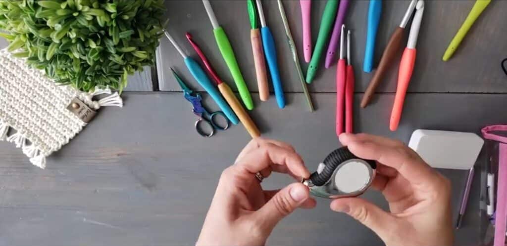 Looking down at a table strewn with crochet hooks in every color, a small scissors and other tools while the instructor holds a small tape measure.