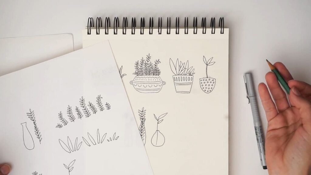 Various sketches of plants in pots and vases are drawn on a notepad. Beside it is a sheet of tracing paper with the same plants, but disassembled into separate elements.