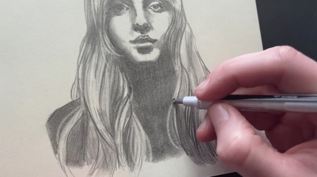 A person's hand using a fine-tipped mechanical eraser to add details to a graphite illustration of a woman with long hair.